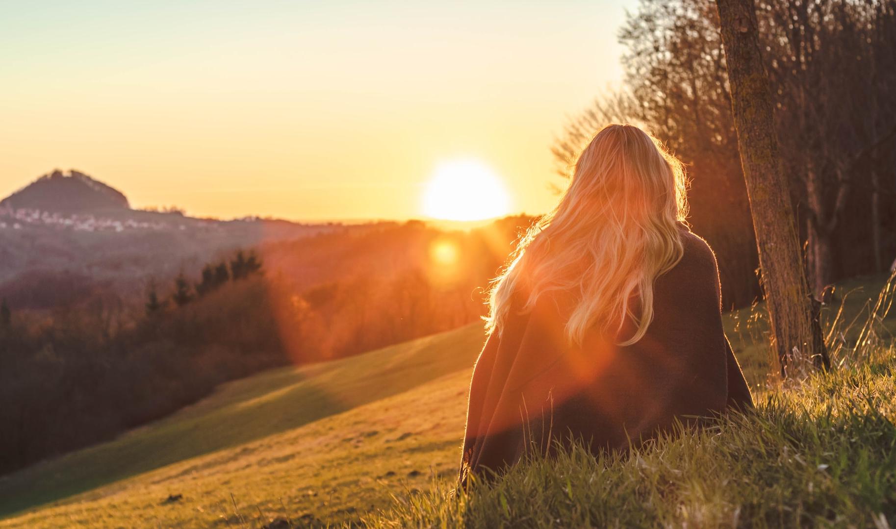 woman sitting on green grass looking at the sun